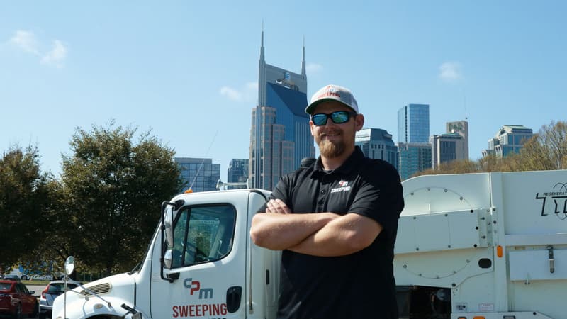 Logan Brasher standing in front of a CPM sweeper truck with the Nashville skyline behind him